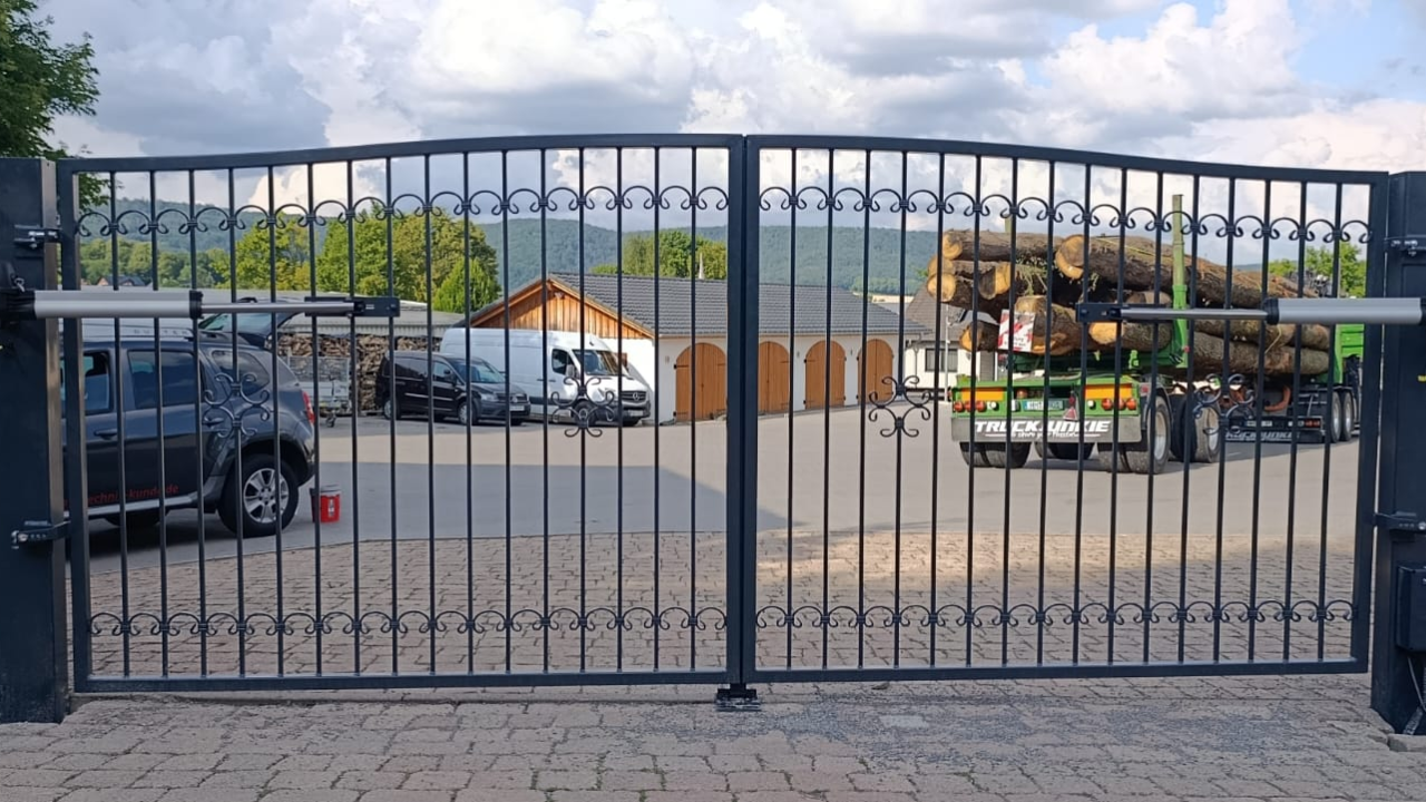 Schmiedeeisernes Flügeltor mit automatischem Antrieb auf einem gepflasterten Hof.