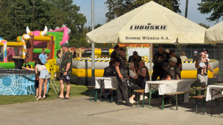 Besucher sitzen an Tischen unter Sonnenschirmen, im Hintergrund gibt es Attraktionen für Kinder